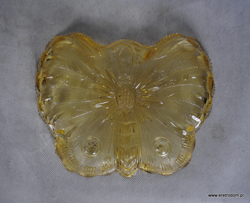 Patera Motyl wyprodukowana w HSG Ząbkowice, nr 1078. Szkło prasowane, barwione w masie na delikatny żółty kolor. Wymiary: 23 cm x 19 cm Stan bardzo dobry, drobne ryski i odpryski powstałe z biegiem lat.